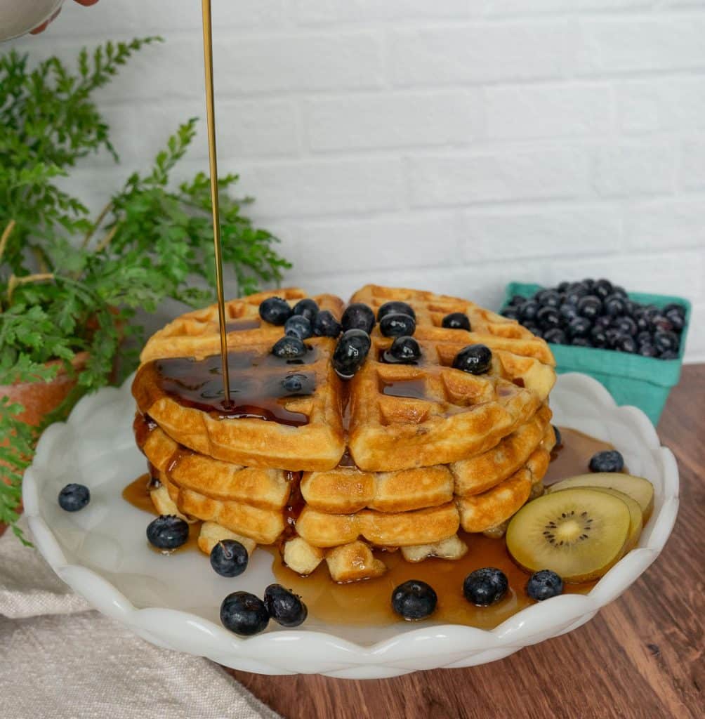 stack of waffles on a plate with syrup being poured over the top of the waffles 