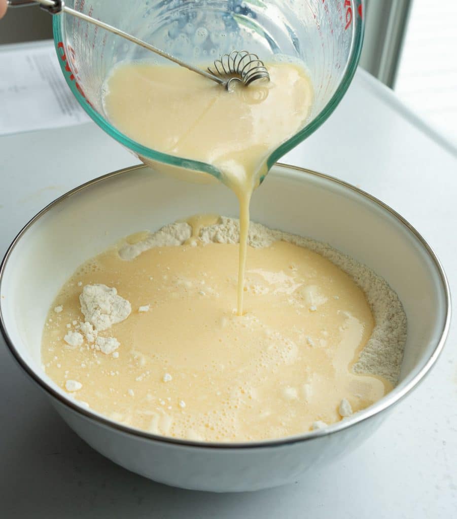 combining wet and dry ingredients. pouring from a large measuring cup into a white bowl with the dry ingredients on a gray table top