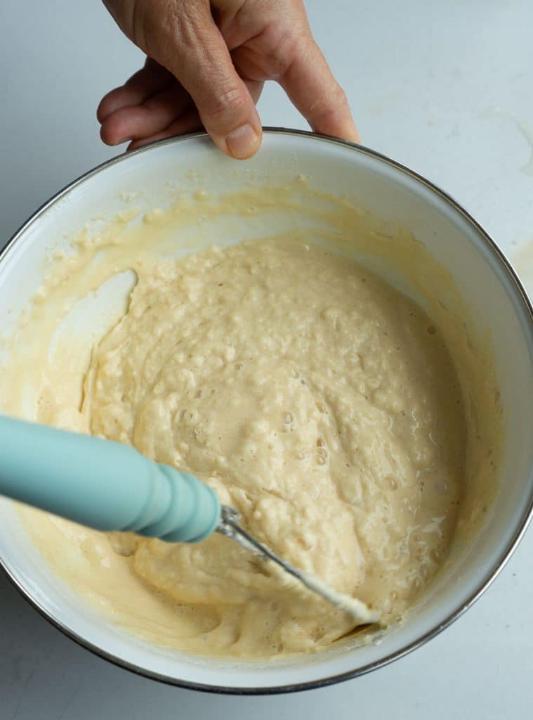 mixing waffle batter with a bread dough whisk in a white bowl on a gray countertop