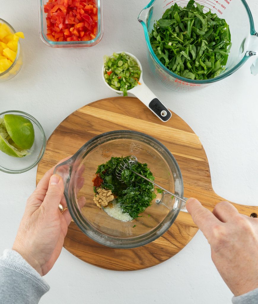 dressing ingredients in a glass bowl, is on top of a wood cutting board, dressing is being whisked 