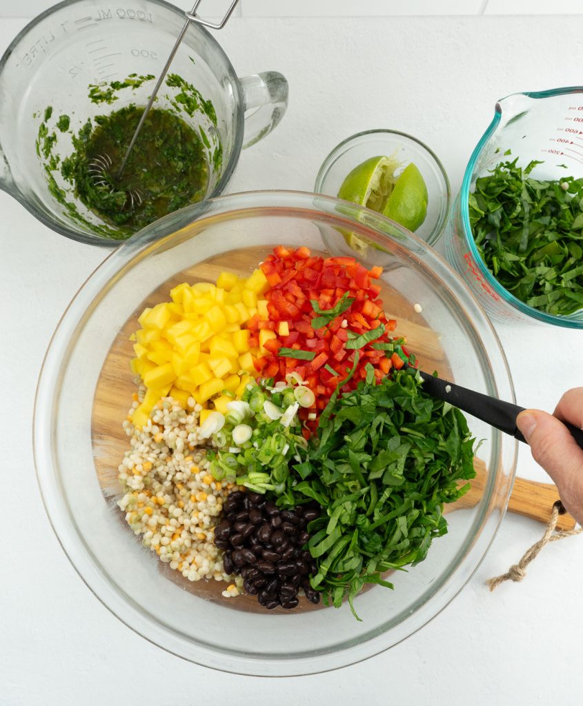 couscous, red bell pepper, mango, green onion, and spinach in a glass bowl on gray countertop