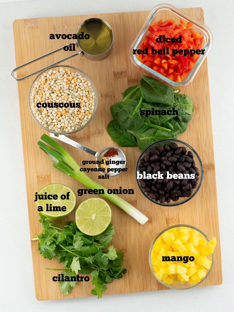 ingredients for mediterranean couscous salad laid out on a wood cutting board and labeled