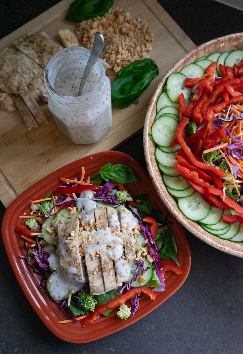 plated thai salad with sliced chicken breast and bowl of salad and jar of salad dressing in the back ground