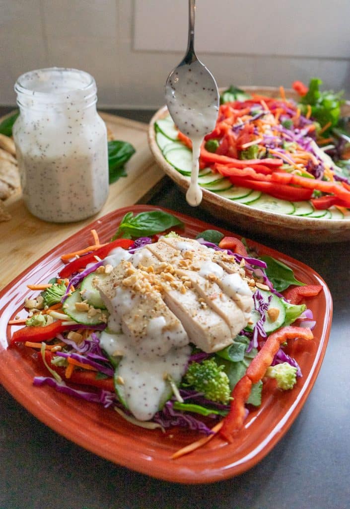plated thai salad with sliced chicken breast and bowl of salad and jar of salad dressing in the back ground