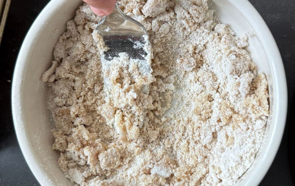 brown sugar and butter crumble in a small cream colored bowl. fork is cutting butter into sugar