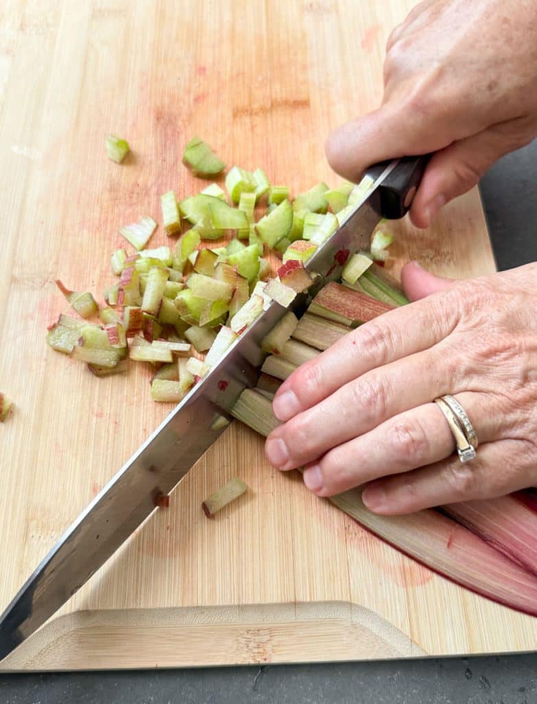cutting rhubarb into small chunks on a wood cutting board