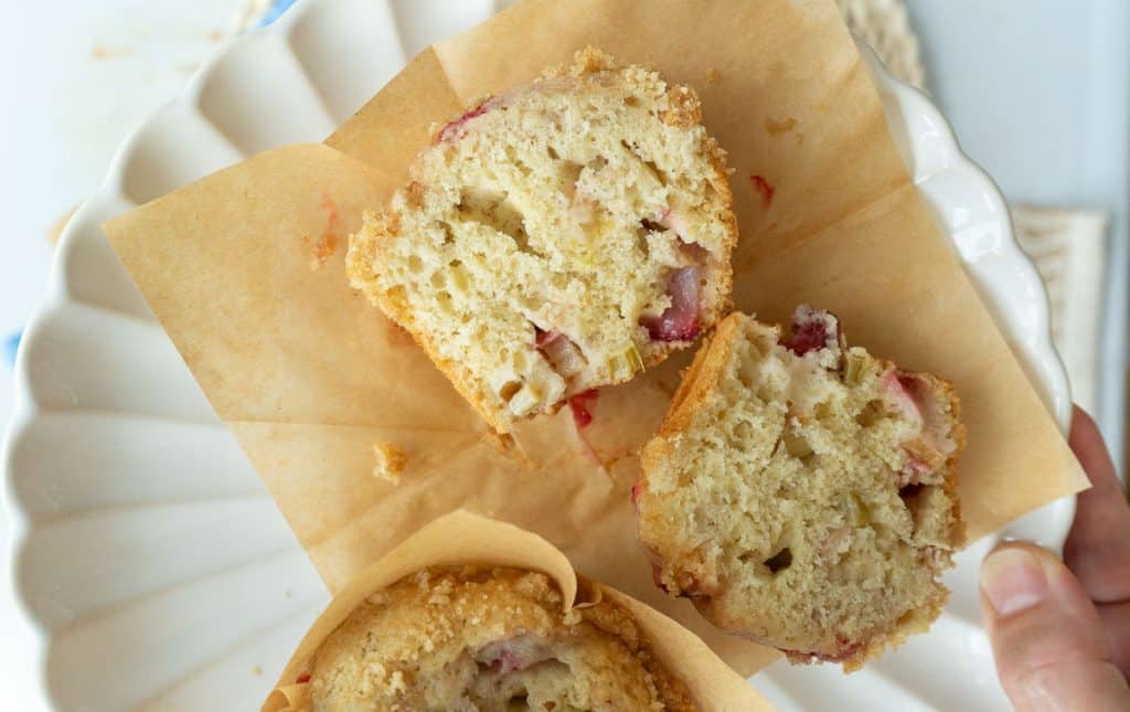 strawberry rhubarb muffin cut in half on a white plate on a white countertop