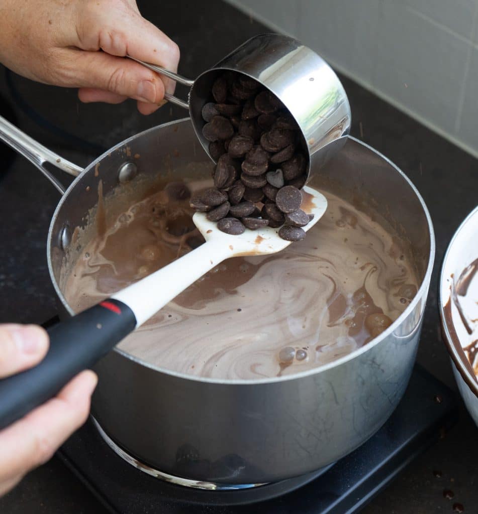 adding dark chocolate chips to the brownie batter ice cream base with a spatula and a measuring cup