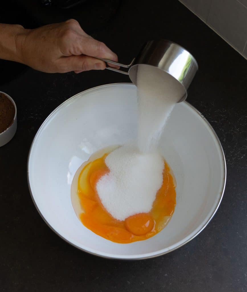 Collage adding sugar to eggs and egg yolks in a white bowl on a black countertop