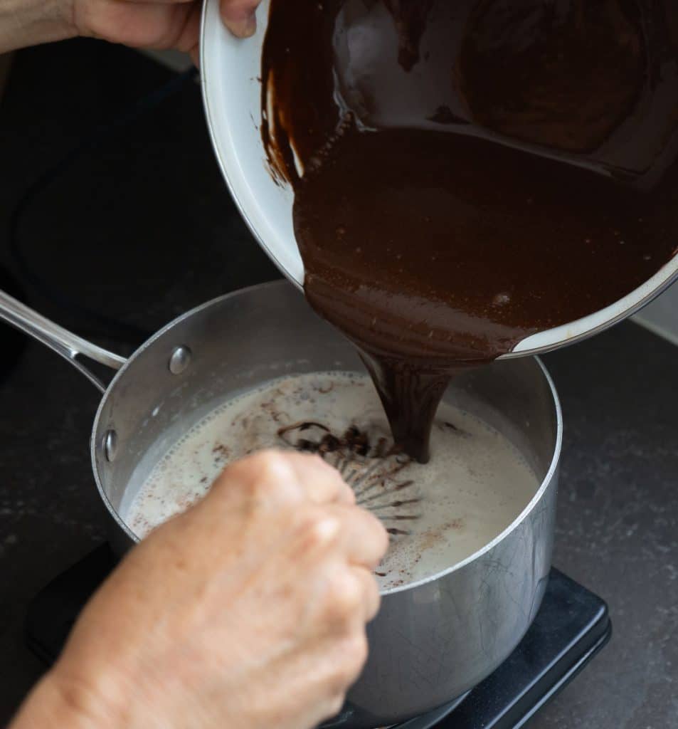 pouring tempered chocolate and egg mixture back into the remaining hot cream on the burner