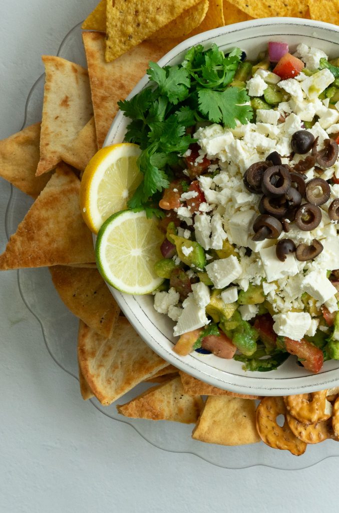 dish of greek quacamole garnished with cilantro, feta, and black olives, surrounded with pita chips