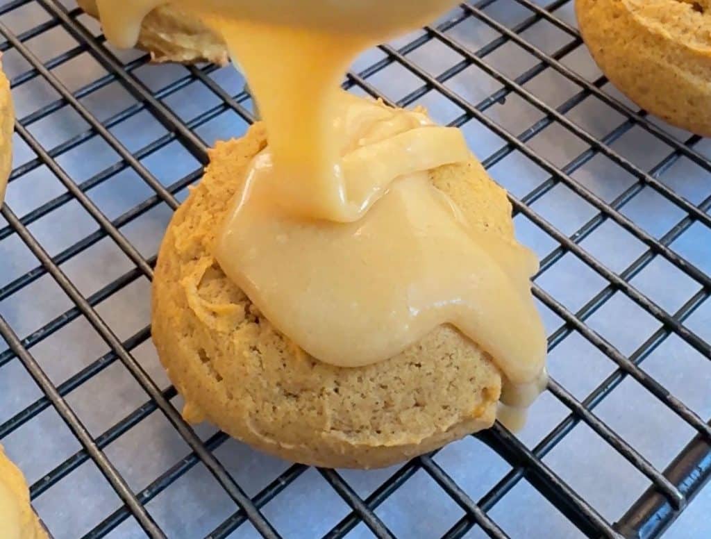 frosting pumpkin spice cookies with caramel frosting on a wire rack