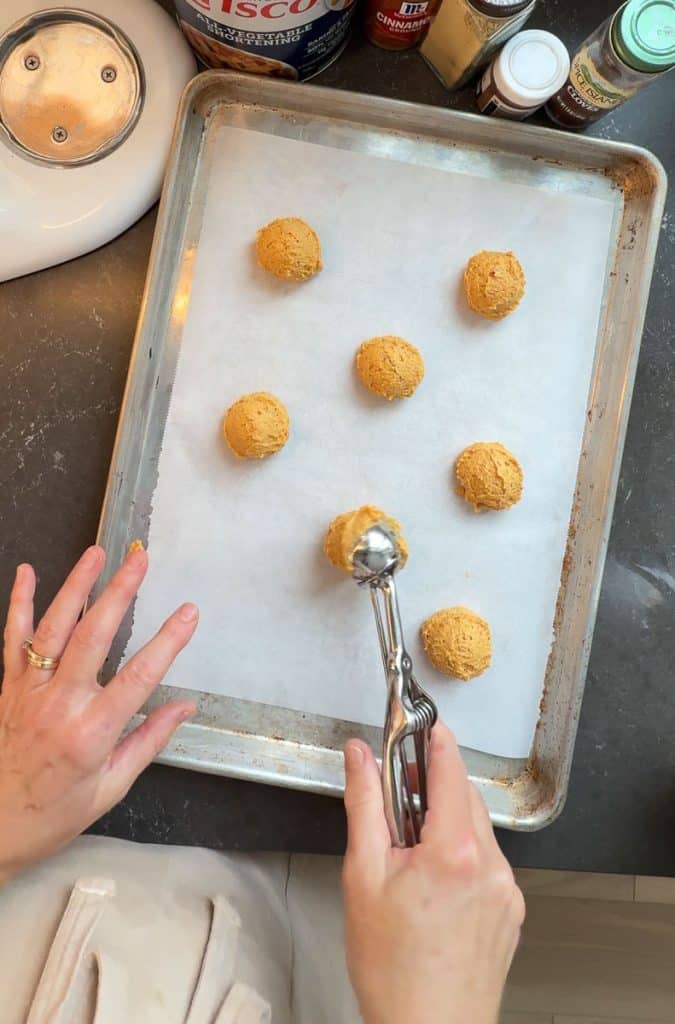 hand scooping cookie dough out on to a parchment line cookie sheet