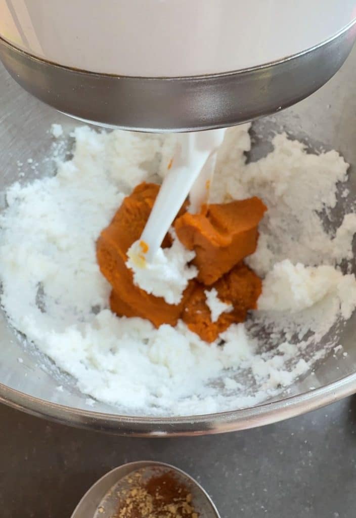 adding pumpkin to mixing bowl with shortening and sugar mixture