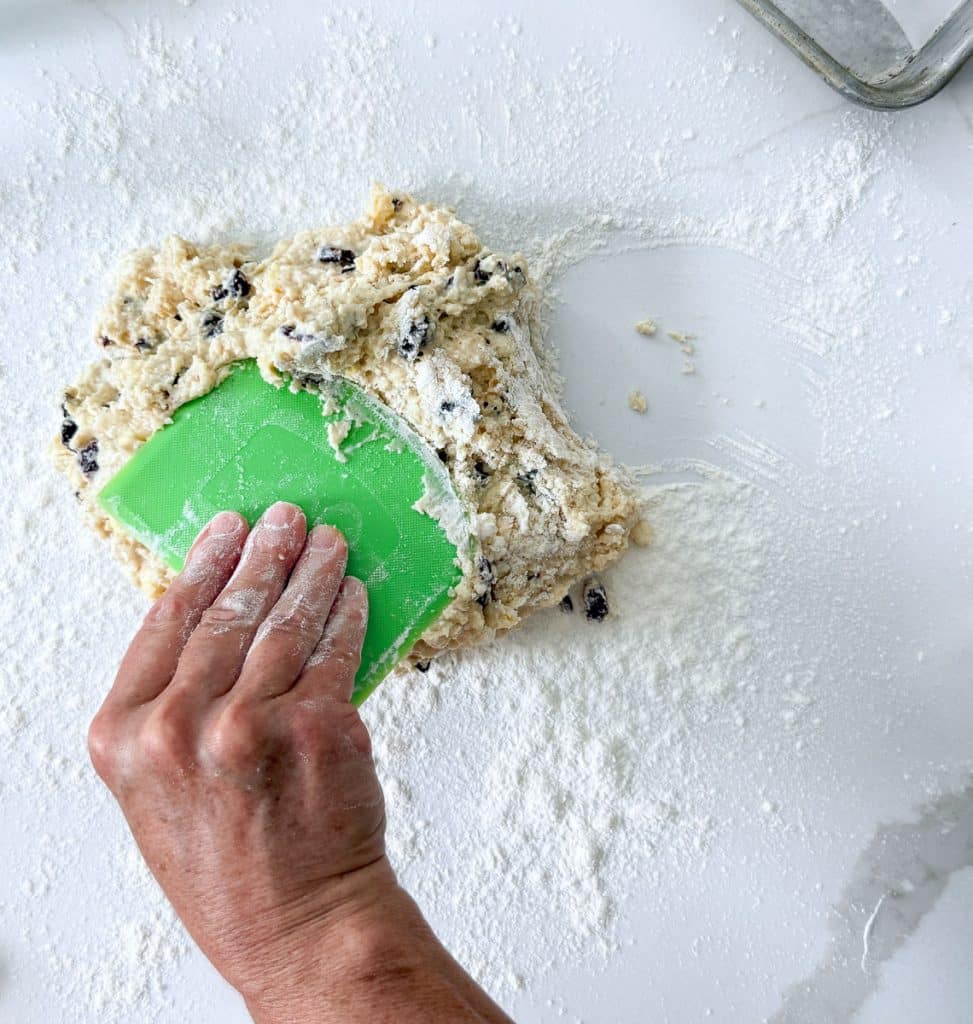 mixing scone dough on counter top with a bread scraper