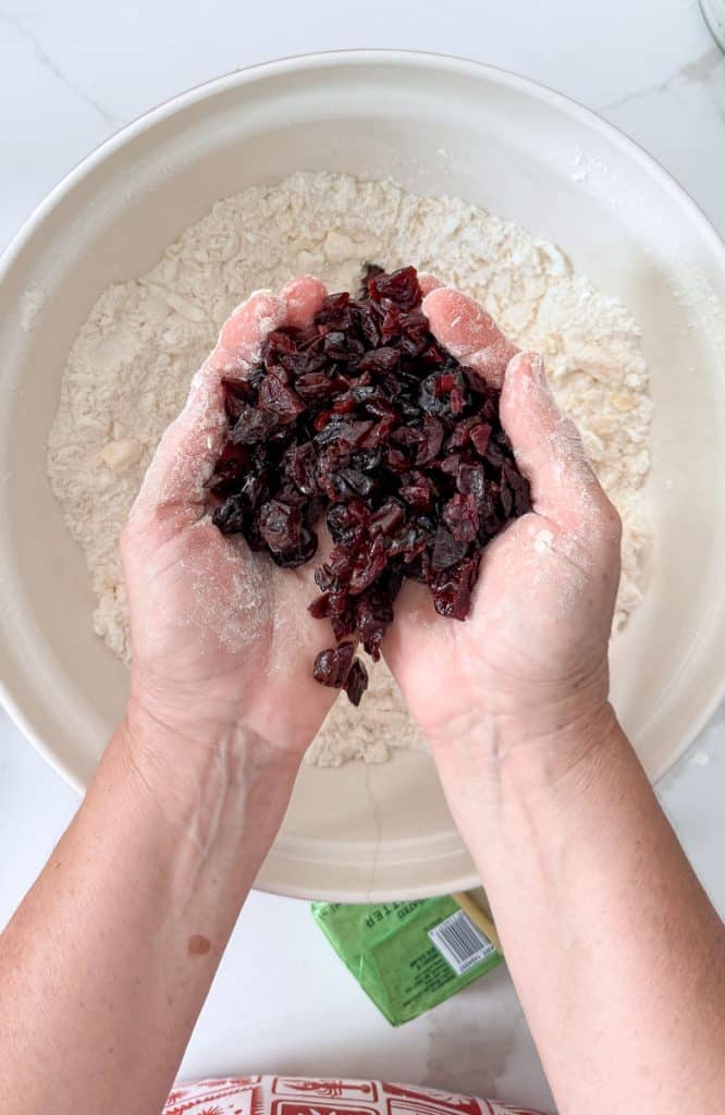 adding chopped dried cherries to the scone ingredients. hands are holding the chopped cherries over bowl