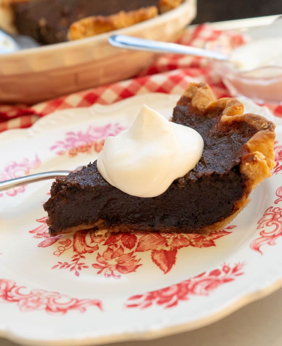 slice of chocolate pie with a dollop of whipped cream on a dessert. plate with the whole pie in the background