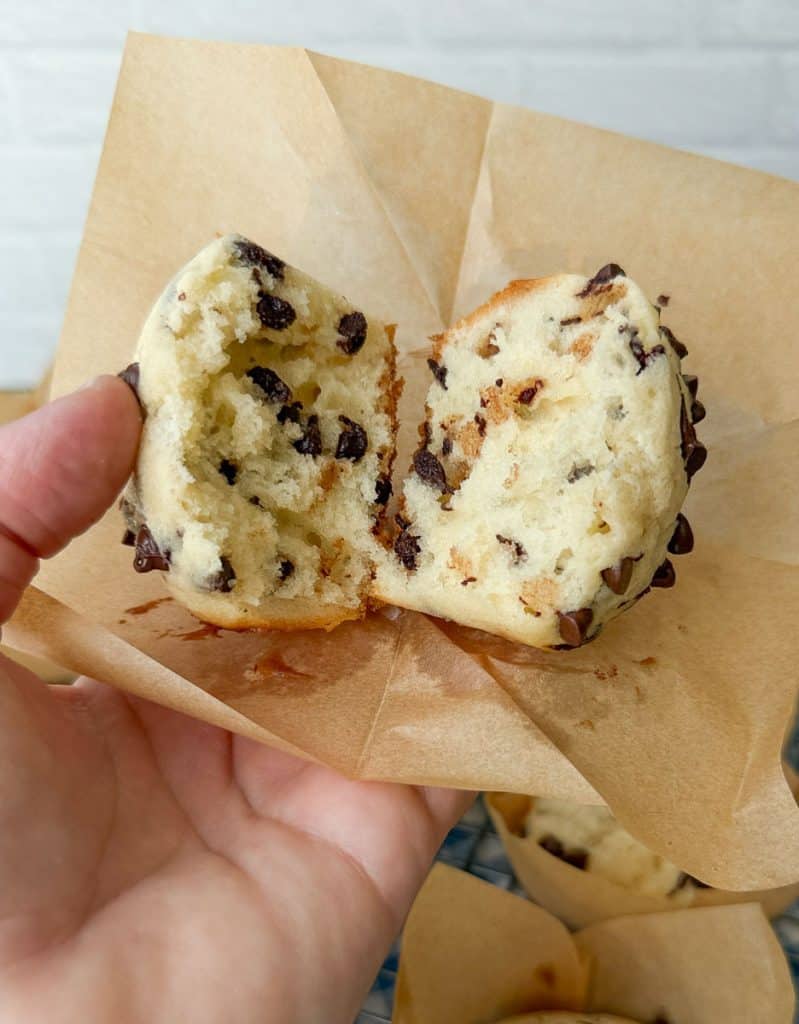 chocolate chip muffin cracked open on a brown paper muffin wrapper