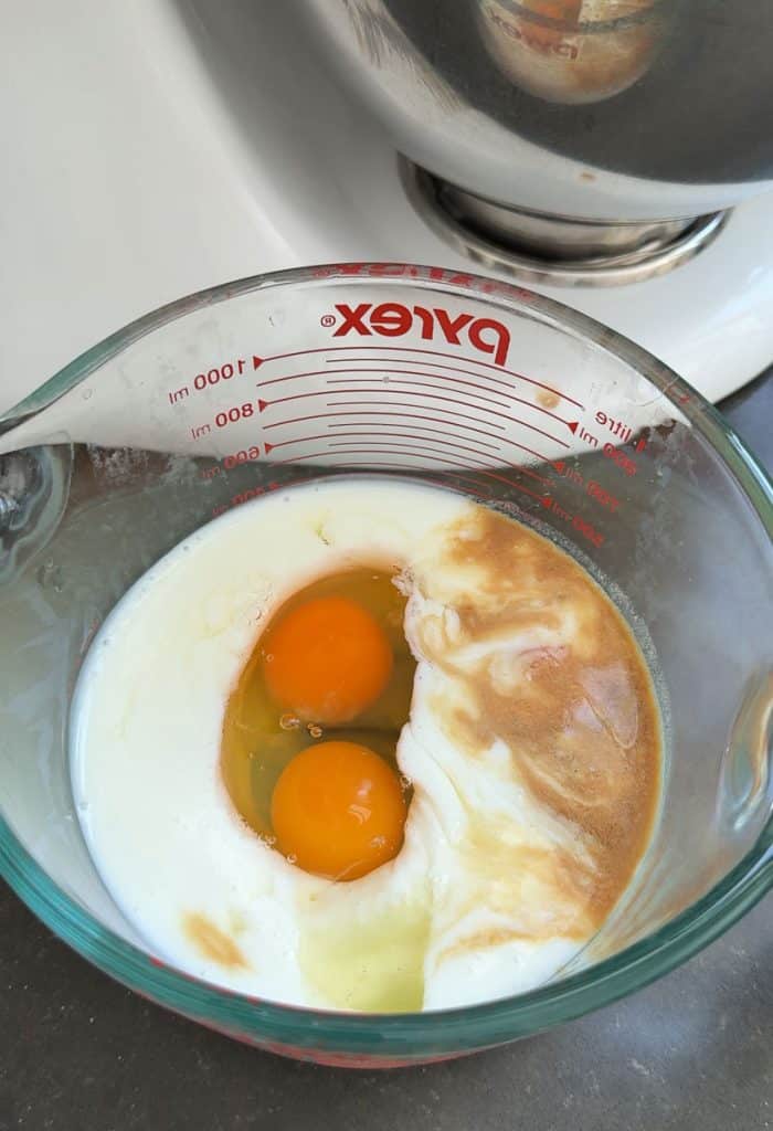 wet ingredients in a glass measuring cup next to stand mixer on a black counter top