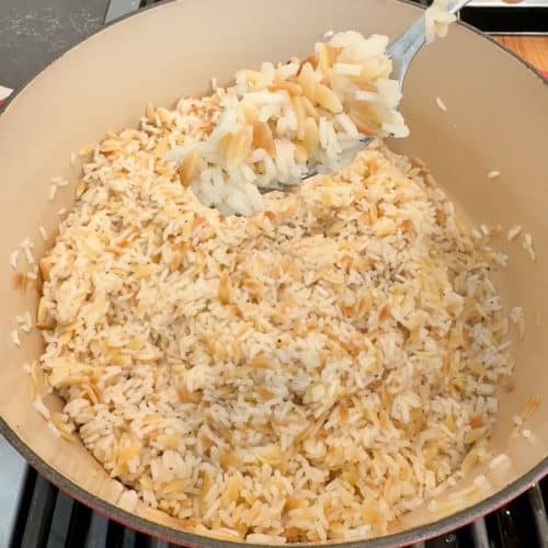 rice pilaf in a pan with a spoon with rice pilaf is held over the pot