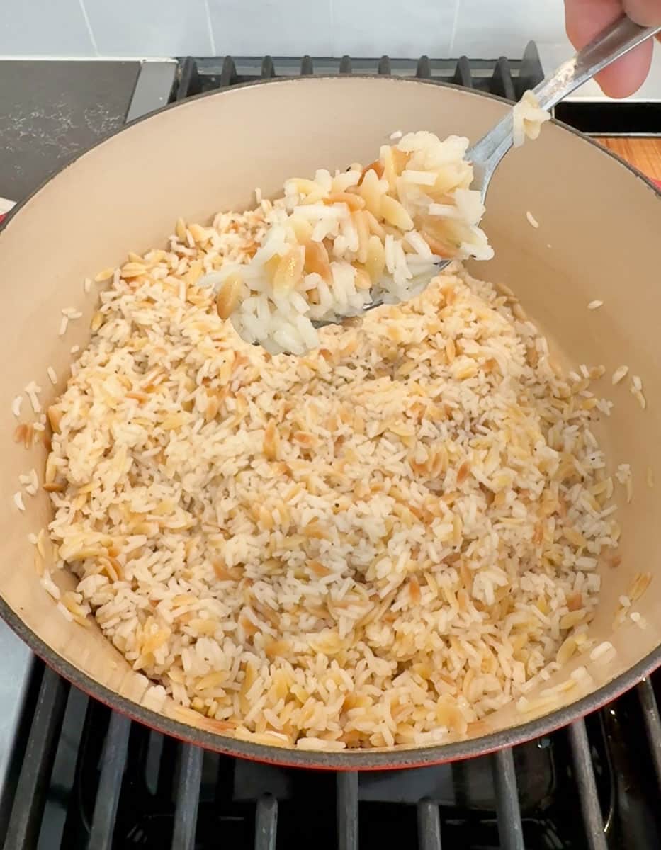 rice pilaf in a pan with a spoon with rice pilaf is held over the pot