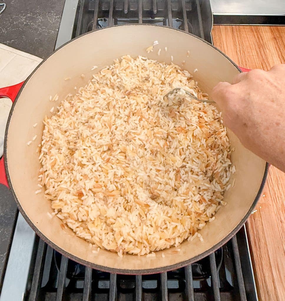 fluffing rice pilaf with a fork in pan on stove top