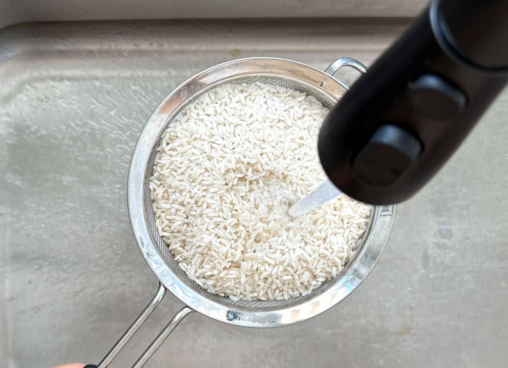 rinsing white rice in a sieve over sink