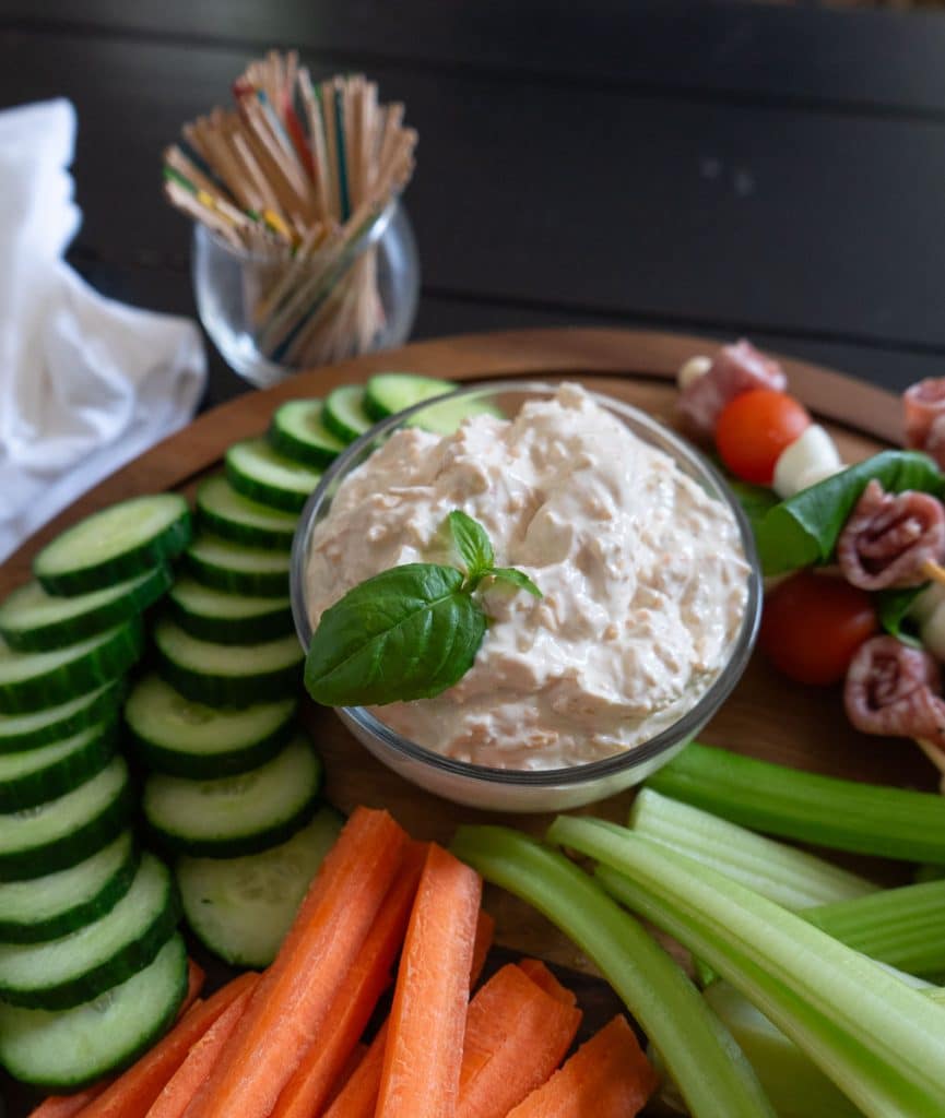 bowl full of vegetable dip with basil for garnish surrounded by fresh cut vegetables