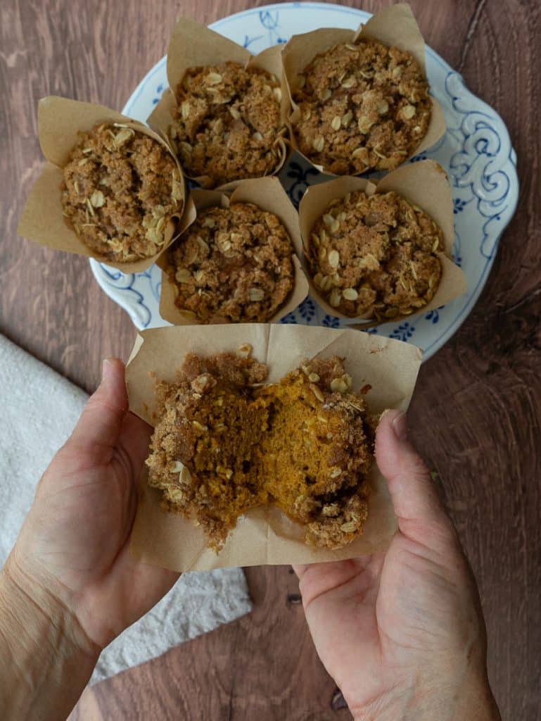 plate of muffins, with hands breaking a muffin in half in the bottom half of the photo