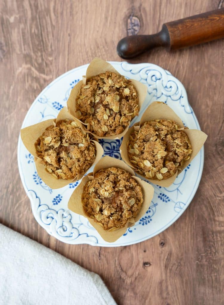 plate of whole wheat pumpkin oatmeal muffins on a wood countertop with a rolling pin in the upper right hand corner and a cloth in the lower left hand corner