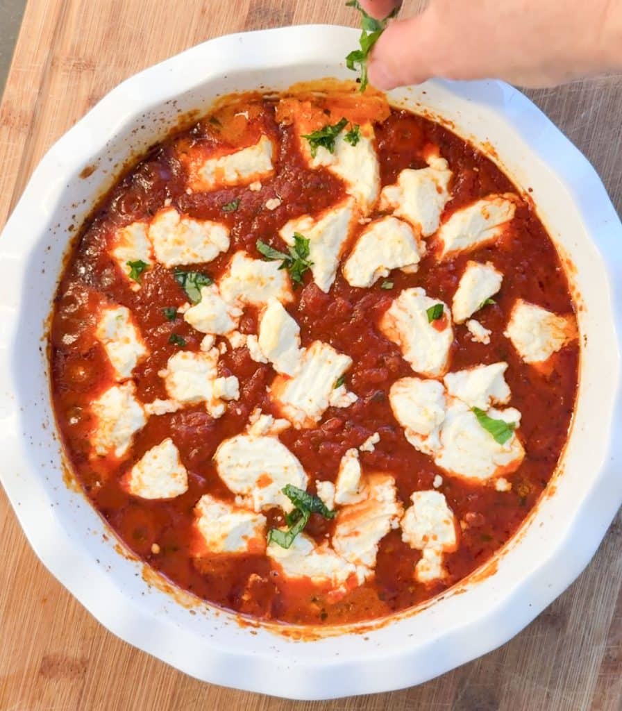 hand sprinkling fresh chopped basil over warm italian goat cheese dip