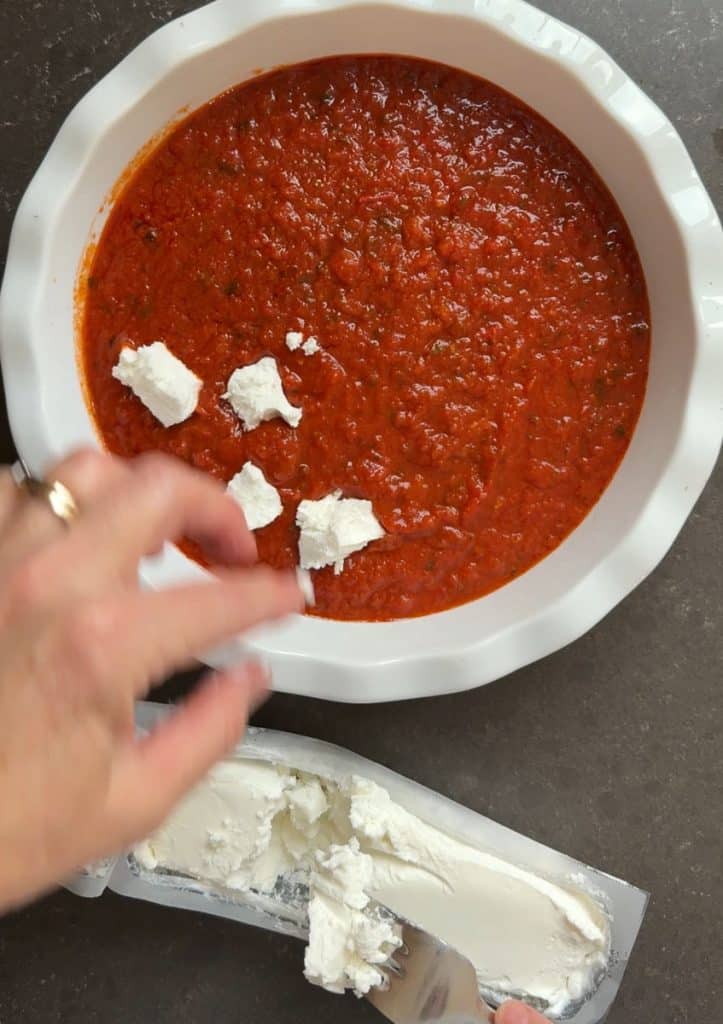 IMG_4256 crumbling goat cheese over marinara sauce in baking dish log of goat cheese is below the baking dish on the counter