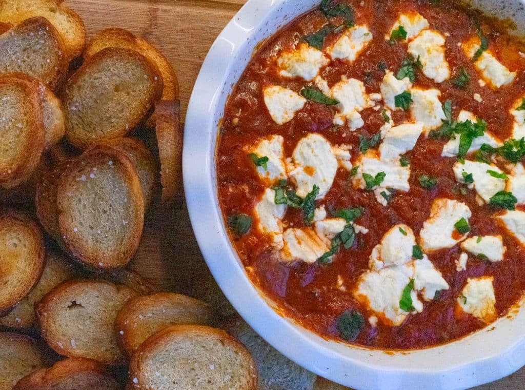 IMG_4261 white dish with marinara and goat cheese dip surrounded with crostini on a wood serving board