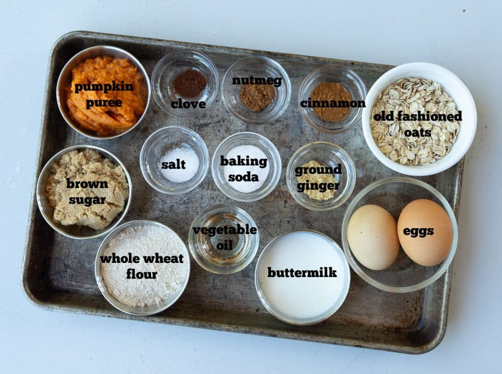 ingredients for whole wheat pumpkin oatmeal muffins on a baking sheet that is on a white countertop