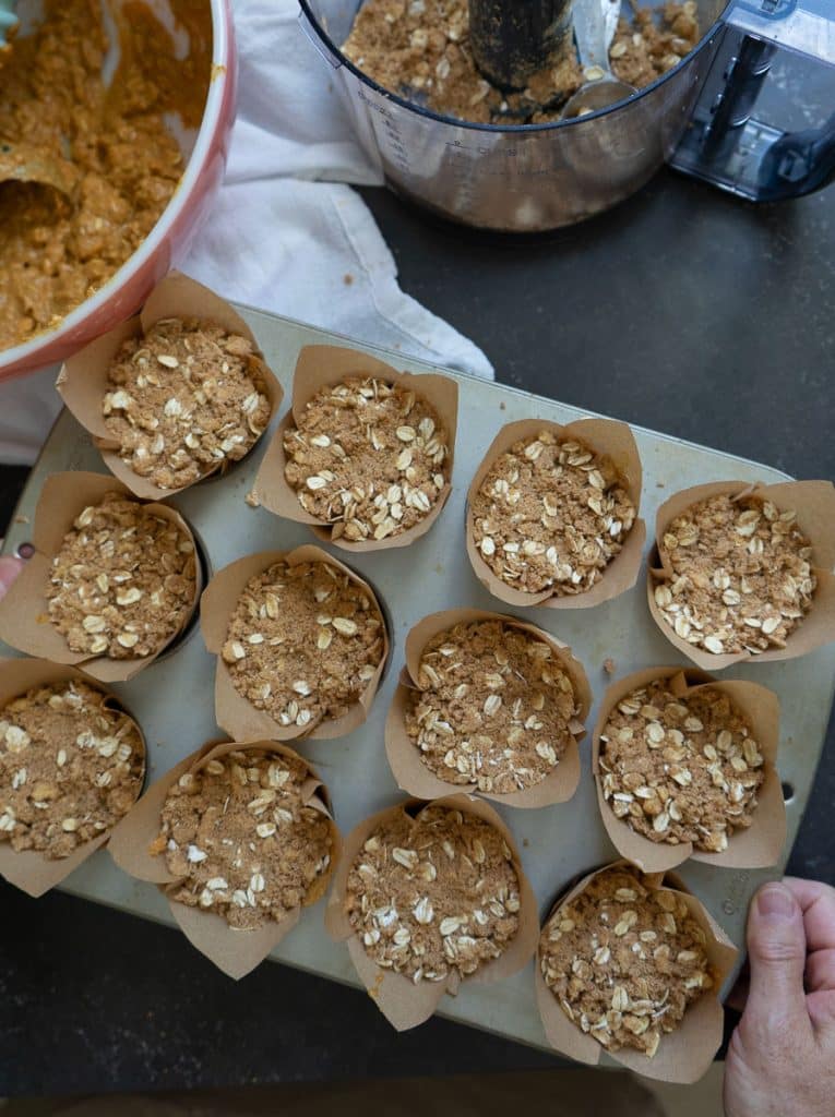 muffin tin full of unbaked whole wheat pumpkin oatmeal muffins on a black countertop