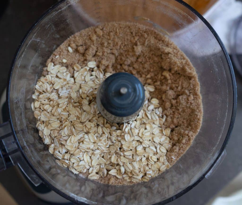 oatmeal sitting on top of crumble mixture in the bowl of food processor