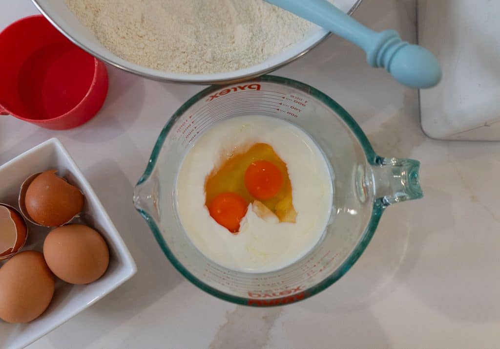 eggs in buttermilk, eggs off to the left side in a white dish, above is large bowl with sifted flour in it with a whisk sticking out