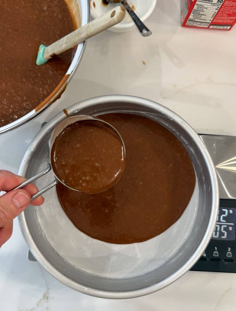 measuring cake batter into prepared round cake pans