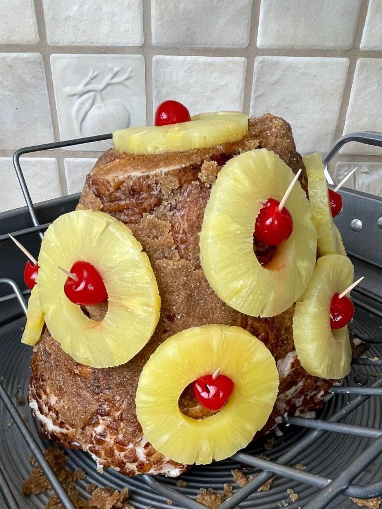 ham with pineapple and maraschino cherries covering it in a pattern in a roasting pan, uncooked