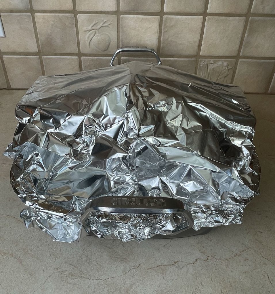ham in roasting pan covered in aluminum foil sitting on kitchen counter top