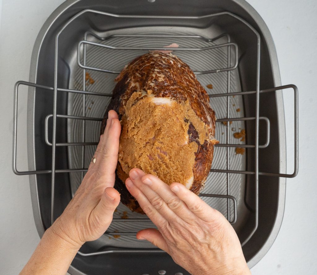 applying brown sugar glaze to ham in a large shallow roasting pan