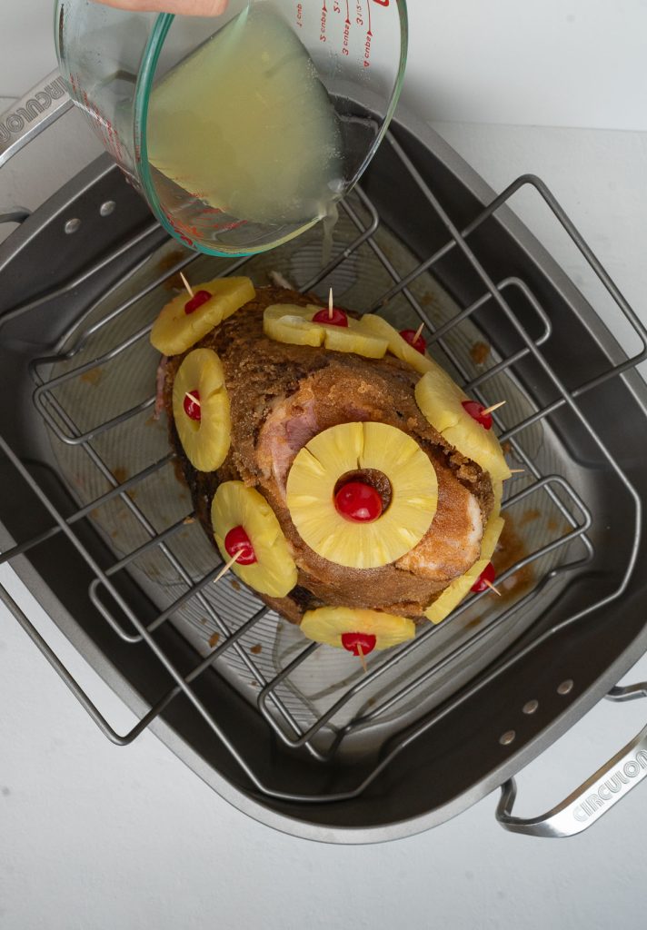 pineapple and brown sugar glazed ham, shown from above with ginger ale being poured into bottom of the pan