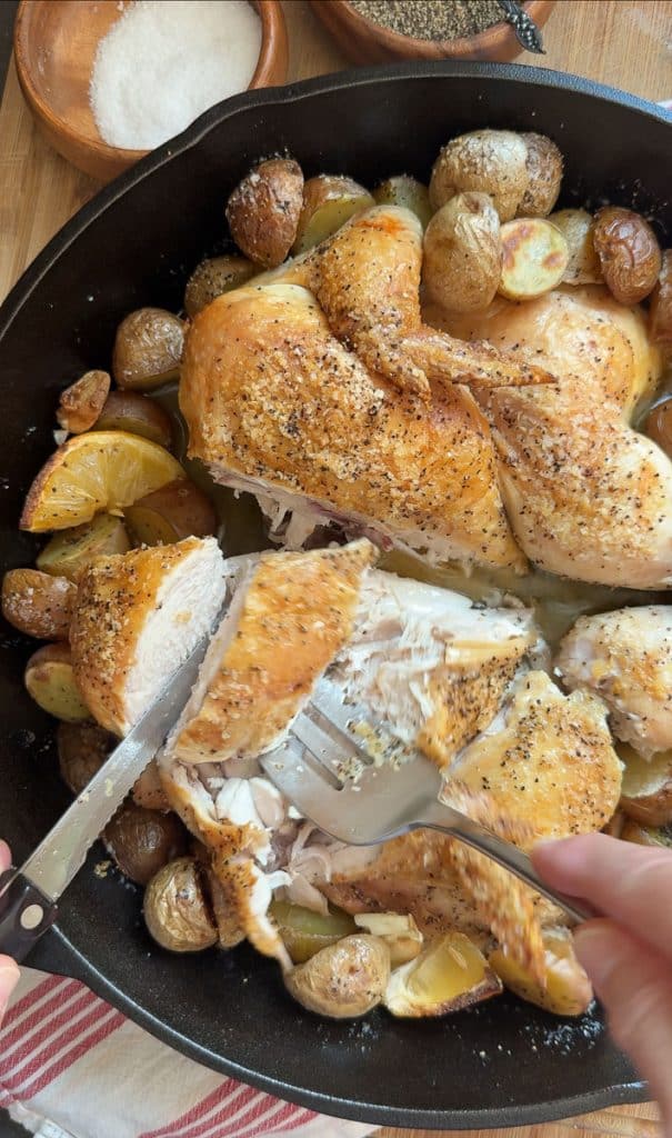 Cutting up roasted chicken that is in a cast iron skillet sitting on kitchen countertop