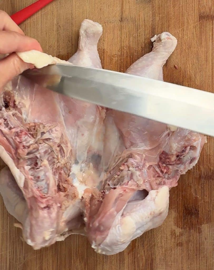trimming some fat and other innards out of the inside of the raw whole chicken  with a knife on a wood cutting board