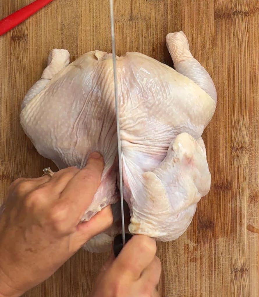 cutting whole chicken along the backbone for spatchcocking 