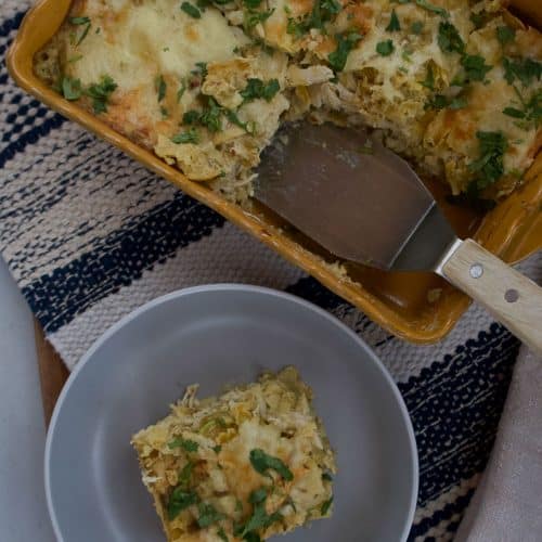 a piece of chicken enchiladas verde on a grey plate with the dish with the rest of the enchiladas in it on a blue and tan place mat
