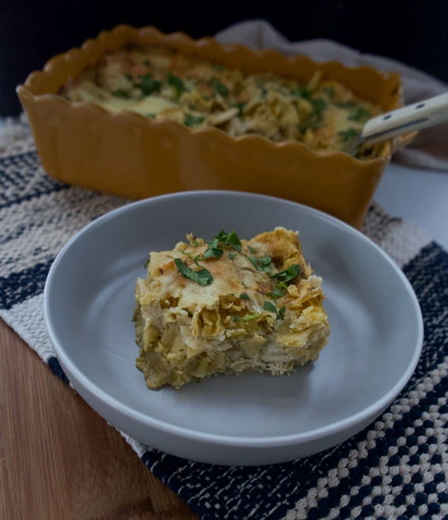 IMG_6025 a piece of chicken enchiladas verde in a gray dish with the pan of enchiladas in the back ground