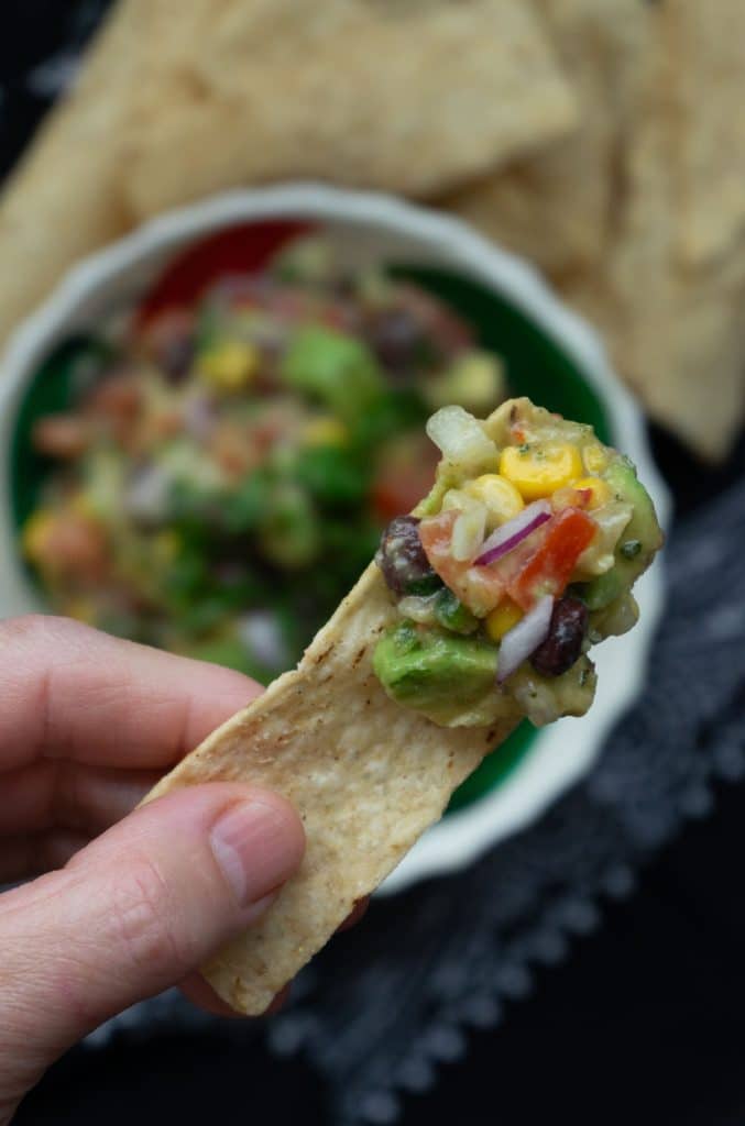 cowboy caviar on a tortilla chip held by a hand over a dish of cowboy caviar and chips on a plate