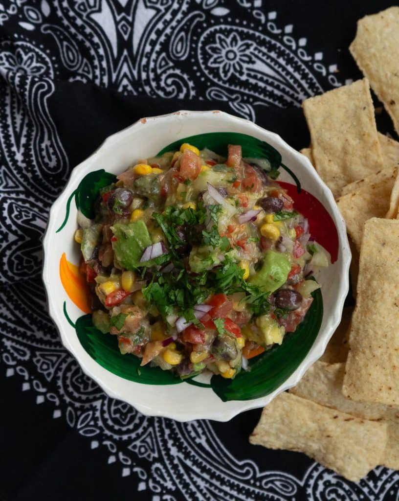 bowl of cowboy caviar with tortilla chips on the side on a black bandana napkin
