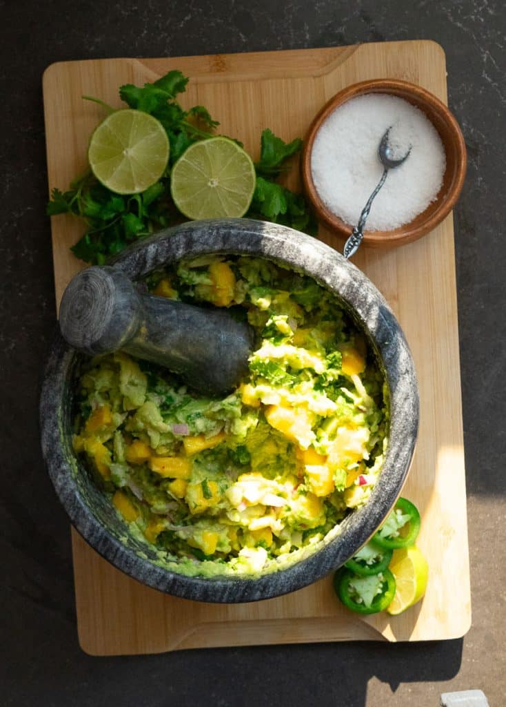stone dish with mango guacamole salad in it with fresh cilantro and lime with a dish of salt dispayed above the bowl